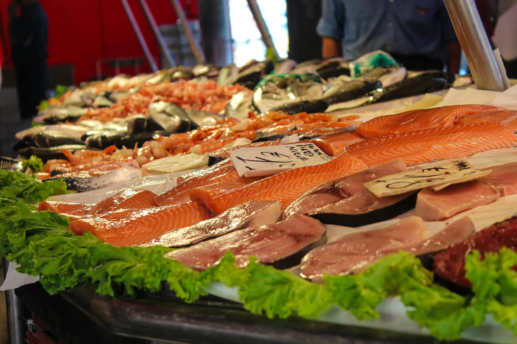 A variety of fresh seafood on display at a market stand with leafy greens, perfect for culinary inspiration.
